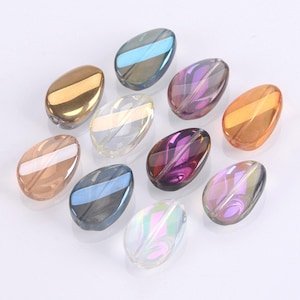 May include: Assortment of iridescent glass beads in various colours, including gold, purple, blue, and clear. The beads are shaped like teardrops and have a smooth, polished finish.