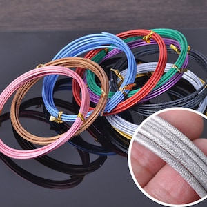 Könnte beinhalten: Sortiment aus farbigem Metalldraht in verschiedenen Farben, darunter rosa, blau, grün, rot, gold, silber und schwarz. Der Draht ist kreisförmig angeordnet und eignet sich perfekt zum Basteln von Schmuck oder anderen Projekten.