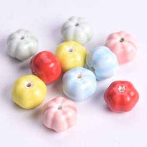 Pode incluir: Conjunto de contas de cerâmica em várias cores, incluindo vermelho, amarelo, azul, verde e rosa. As contas têm a forma de pequenas abóboras com um furo no centro para enfiar.