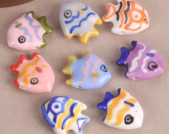 May include: Assortment of colorful ceramic fish beads with painted details. Each bead features a different color and pattern, including blue, pink, purple, yellow, and orange.