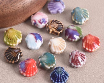 May include: A collection of ceramic seashell beads in various colors, including blue, red, white, and brown. The beads have a glossy finish and are arranged on a neutral surface. These decorative beads are ideal for jewelry making and craft projects.
