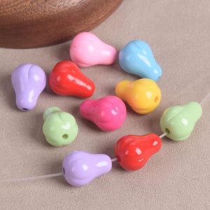 Puede incluir: Una colección de cuentas coloridas en forma de pera en varios tonos, incluyendo rosa, rojo, amarillo, verde, azul y morado. Las cuentas están ensartadas en un cordón fino y transparente, para bisutería o manualidades.