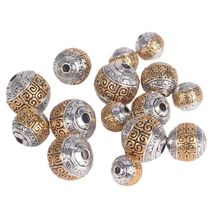 May include: A collection of round, gold and silver beads with an intricate geometric pattern. The beads have a hole in the centre for stringing.