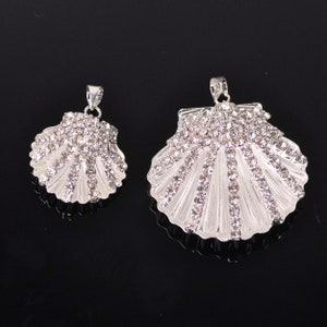 May include: Two silver tone shell-shaped pendants with clear rhinestones. The larger pendant is about 2 inches wide and the smaller pendant is about 1 inch wide.