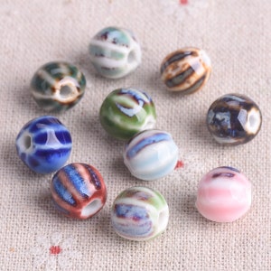 May include: Assortment of ceramic beads with various colourful striped patterns. The beads are round and have a hole in the centre for stringing.