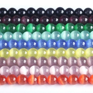 May include: A strand of round, smooth, cat's eye beads in various colours, including black, purple, green, blue, yellow, pink, and red.