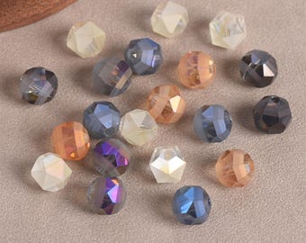 May include: A collection of small, multifaceted glass beads in various colors including translucent white, soft peach, deep blue, and dark grey. Each bead features a geometric, faceted surface that reflects light, scattered across a neutral surface.