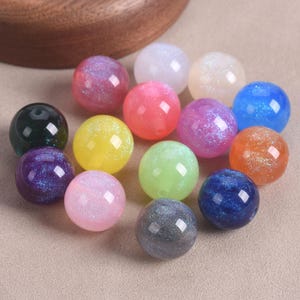 Può includere: Una collezione di perline rotonde e colorate in varie tonalità, tra cui rosa, blu, verde, giallo e viola. Alcune perline hanno un effetto glitterato e iridescente. Le perline sono lisce e sembrano essere fatte di vetro o materiale simile.