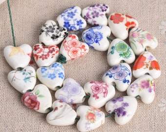 Può includere: Una collana di perline di ceramica bianca a forma di cuore con vari motivi floreali in tonalità di blu, rosso, verde e viola.