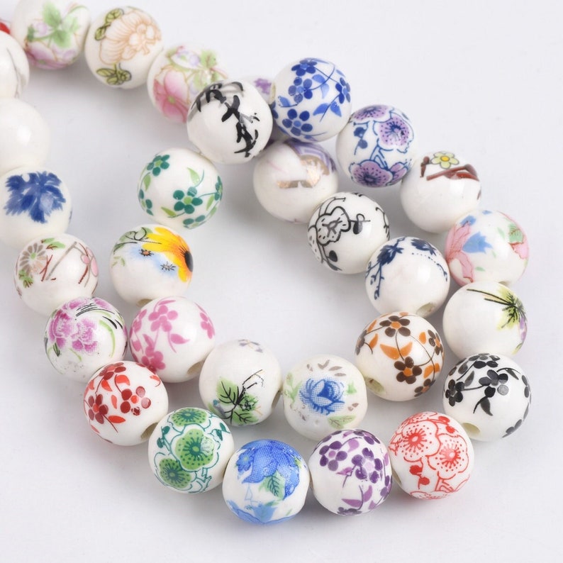 May include: A strand of white ceramic beads with various floral patterns in shades of blue, red, green, and yellow.