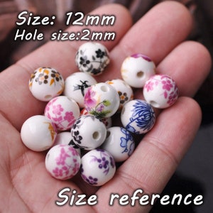 May include: A collection of 12 mm white ceramic beads with floral patterns in various colors. The beads have a 2 mm hole for stringing.