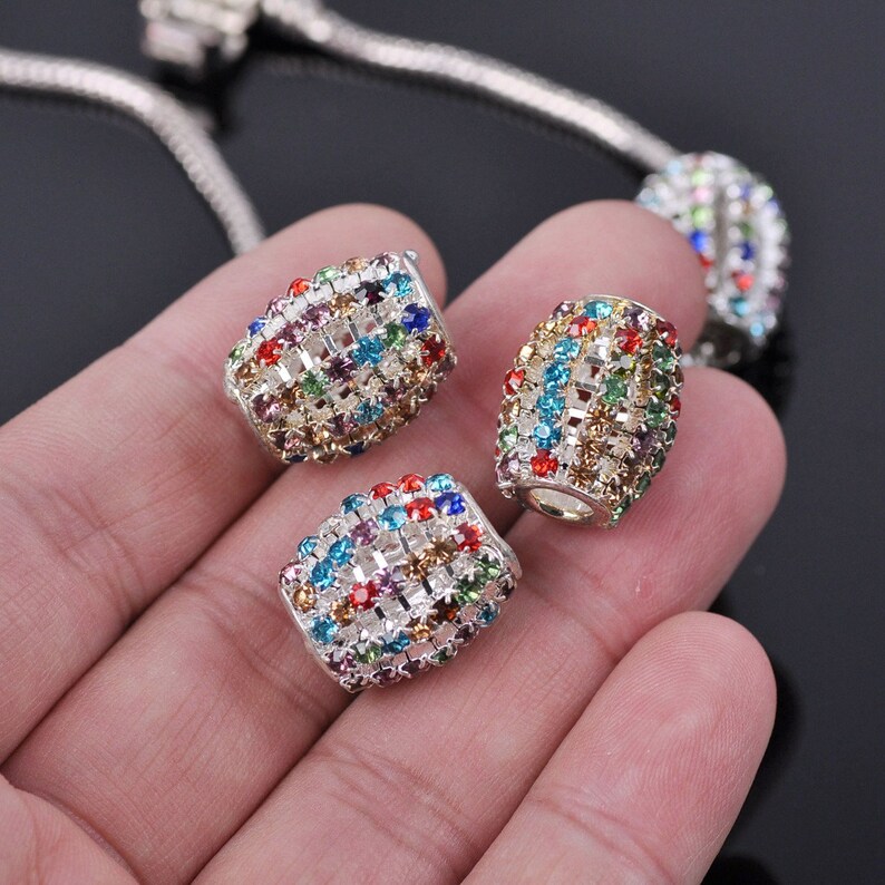 May include: Three silver charm beads with a colorful, multi-faceted crystal design. Each bead is a cylinder shape with a grid pattern.