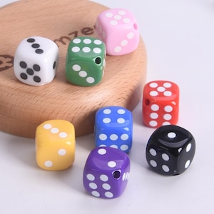 May include: A collection of colorful dice in various colors, including white, pink, green, yellow, blue, purple, red, and black. Each die has white dots representing numbers. The dice are arranged on a wooden surface.
