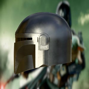 May include: A metallic gray Mandalorian helmet with a T-shaped visor and a silver-colored vertical accent. The helmet has a smooth, reflective surface and a distinctive, angular design, suggesting a sci-fi or cosplay theme.