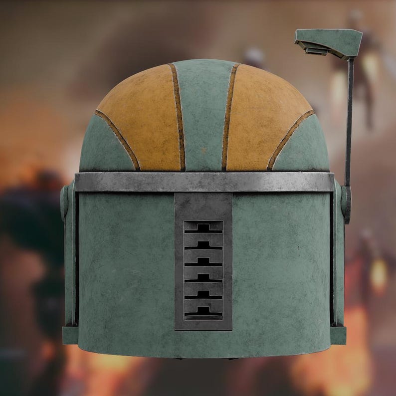 Op de afbeelding: Een verweerde helm met een saliegroene koepel met mosterdgele panelen, een metallic zilveren voorhoofdband en een verticaal rechthoekig ventilatierooster aan de voorzijde. Een dunne, L-vormige antenne steekt omhoog aan de rechterkant van de helm.