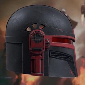 May include: A matte black helmet featuring deep red accents along the visor and side panels. The design includes a horizontal red visor slit, a vented section below the eye area, and a prominent circular mechanical detail on the side.
