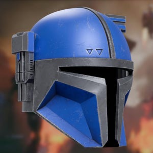 Op de afbeelding: Een blauwe helm met een verweerd, metaalgrijs T-vormig vizier en rand. De helm heeft een gladde, ronde koepel met twee kleine driehoekige uitsparingen boven het vizier en een rechthoekig hulpstuk aan de zijkant met verticale details.
