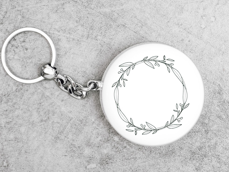 May include: A silver keychain with a round white charm featuring a black line drawing of a floral wreath.