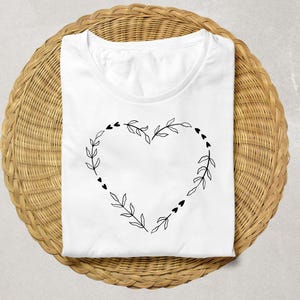 May include: White t-shirt with a black floral heart design. The heart is made of leaves and small hearts.
