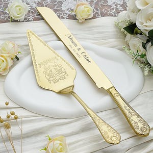 Puede incluir: Un juego de cuchillo y servidor de pastel de color dorado. El cuchillo tiene los nombres "Mason & Chloe" y la fecha "Dec. 07, 2025" grabados en la hoja. El servidor y el cuchillo presentan diseños florales y de volutas ornamentados. El juego se exhibe en una fuente blanca.