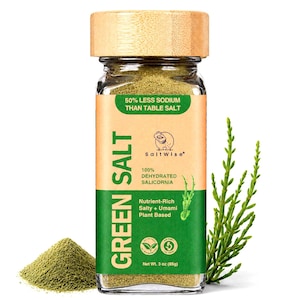 May include: A clear glass jar with a light wood lid containing green salt, labeled Green Salt with 50% less sodium than table salt, 100% dehydrated salicornia, and net weight 3 oz (85g). A small pile of green powder and a green salicornia sprig.
