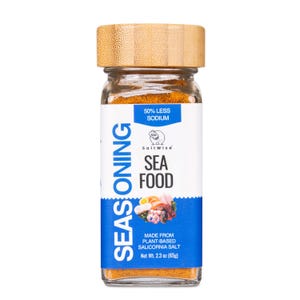 May include: A clear glass jar of SaltWise seafood seasoning with a light brown bamboo lid. The white and blue label features the text "SEASONING", "SEA FOOD", "50% LESS SODIUM", and "MADE FROM PLANT-BASED SALICORNIA SALT" with a net weight of 2.3 oz.