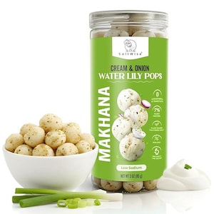 May include: A jar of SaltWise Cream & Onion Water Lily Pops, with a white bowl of the same product. The jar has a green label with product information and the text "MAKHANA". Green onions and a dollop of cream are also visible.
