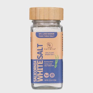 May include: A clear glass jar filled with white salt, topped with a light brown wooden lid. The label features blue and tan colors with the text Salicornia White Salt, 50% Less Sodium Than Table Salt, 100% Plant Based Salt, and Net Wt. 4.5 oz (128g).