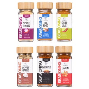May include: Six glass jars of SaltWise seasoning with light wood lids, arranged in two rows. Flavors include Spiced Onion, Sea Food, Chili Lime, Pepper Garlic, Barbecue, and Cajun. Each label displays 50% less sodium, 2.2 oz (62g) net weight.
