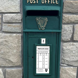 May include: A green metal post box with the words "POST OFFICE" on the front. The post box has a slot for mail and a sign that says "PRIVATE BOX NO COLLECTIONS" with a schedule of collection times.