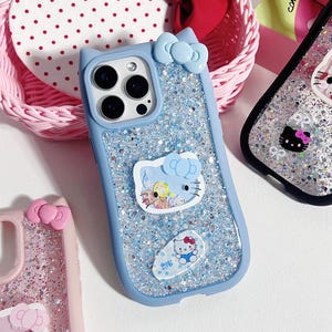May include: A collection of phone cases featuring glitter and cartoon character designs. The cases are in various colors, including blue and pink, and feature a bow and cat ear design. The cases have a glittery background and cartoon character stickers.
