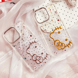 May include: Two clear phone cases with a sparkly background and gold Hello Kitty designs. The cases are decorated with small stars and rhinestones.
