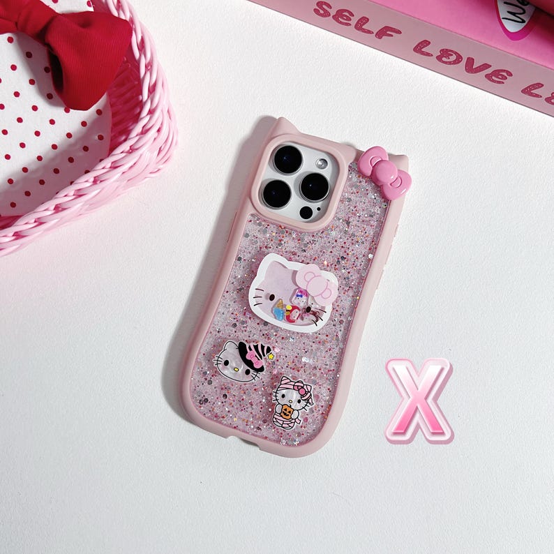 Może przedstawiać: R&oacute;żowe, brokatowe etui na telefon z motywami Hello Kitty. Etui ma kokardkę na g&oacute;rze i kilka wzor&oacute;w postaci Hello Kitty. Etui jest przeznaczone do smartfona.