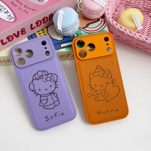 Pu&ograve; includere: Due custodie per telefono, una viola e una arancione, ciascuna con un design di Hello Kitty. La custodia viola ha il nome "Sofia" stampato, mentre la custodia arancione ha "Hanna". Le custodie sono realizzate in un materiale strutturato.