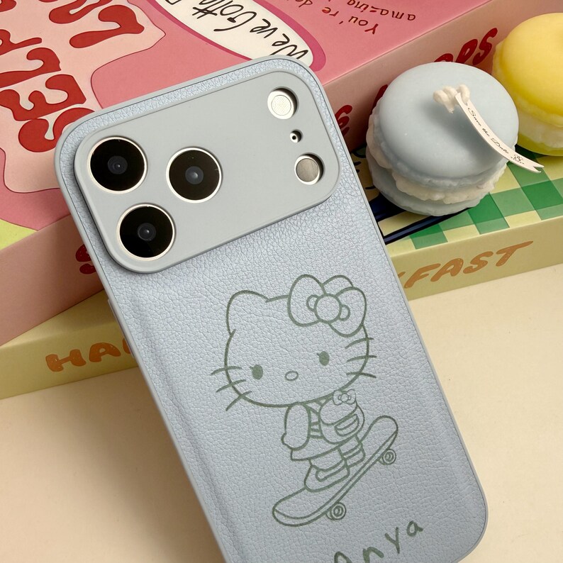 Puede incluir: Funda de tel&eacute;fono azul claro con un dise&ntilde;o de Hello Kitty en monopat&iacute;n. La funda tiene un acabado texturizado y un m&oacute;dulo de c&aacute;mara gris. El nombre "Anya" est&aacute; impreso en la parte inferior.