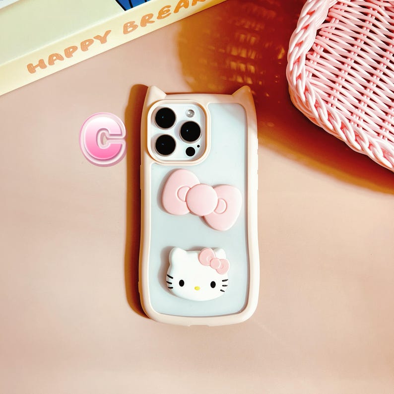 Puede incluir: Una funda de tel&eacute;fono rosa y blanca con un dise&ntilde;o de Hello Kitty. La funda tiene una parte posterior transparente y un lazo rosa en la parte posterior. La funda est&aacute; dise&ntilde;ada para un iPhone.