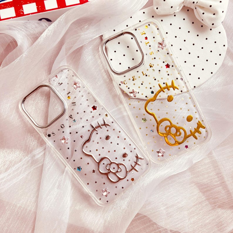 May include: Two clear phone cases with a sparkly background and gold Hello Kitty designs. The cases are decorated with small stars and rhinestones.