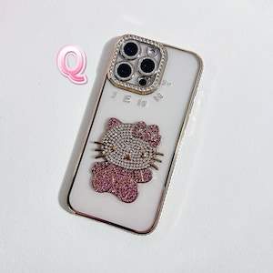 Pu&ograve; includere: Custodia per iPhone bianca con bordo dorato e design Hello Kitty con strass. La custodia ha un retro trasparente e una copertura per l'obiettivo della fotocamera con strass.