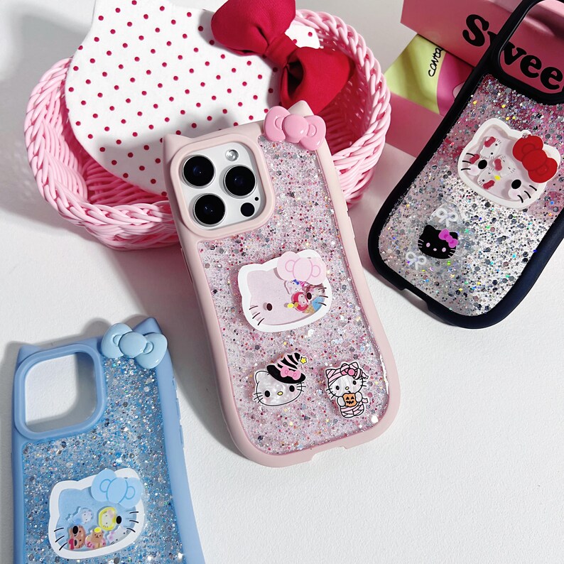 Może przedstawiać: R&oacute;żowe, niebieskie i czarne etui na telefony z brokatem i wzorami Hello Kitty. R&oacute;żowe etui ma kokardkę i kilka naklejek Hello Kitty. Niebieskie etui ma kokardkę i wz&oacute;r Hello Kitty. Czarne etui ma wz&oacute;r Hello Kitty.