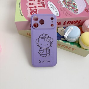 Puede incluir: Una funda de tel&eacute;fono lila con un dise&ntilde;o negro de Hello Kitty con sombrero y lazo, con el nombre "Sofia" debajo. La funda tiene un recorte para la c&aacute;mara. El fondo incluye una caja de cereales y macarons coloridos.