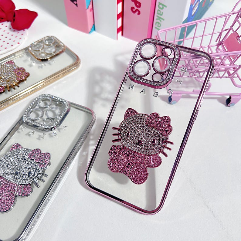 K&ouml;nnte beinhalten: Drei transparente Handyh&uuml;llen mit Strasssteinen und einem Hello-Kitty-Design. Die H&uuml;llen sind rosa, silber und gold. Das Hello-Kitty-Design ist rosa mit Strasssteinen.