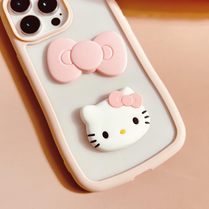 Puede incluir: Una funda de tel&eacute;fono blanca con un lazo rosa y un personaje de Hello Kitty. La funda est&aacute; hecha de un material suave y flexible y tiene una parte posterior transparente.