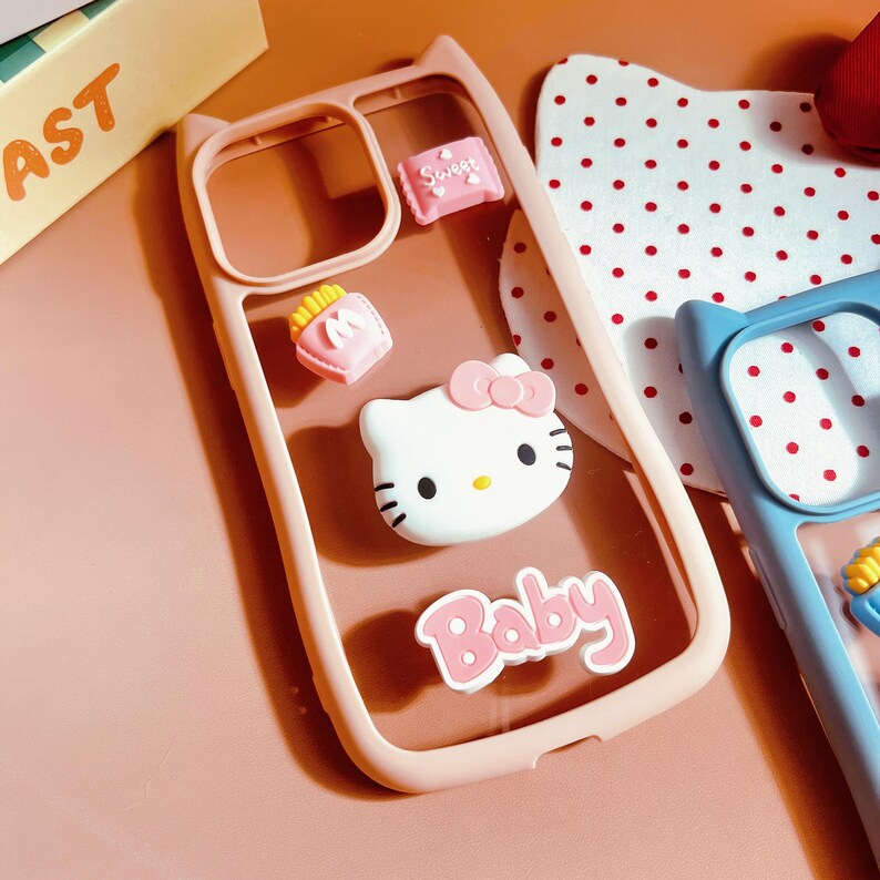 Op de afbeelding: Een roze transparante telefoonhoes met een Hello Kitty-figuur, een zakje friet en een zakje snoep. De hoes heeft de tekst "Baby" erop.
