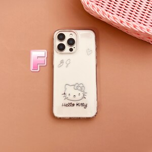 May include: Clear phone case with a white background featuring a Hello Kitty design. The case has a silver outline and includes the text "Hello Kitty". Additional silver embellishments include a heart and the letters "88".