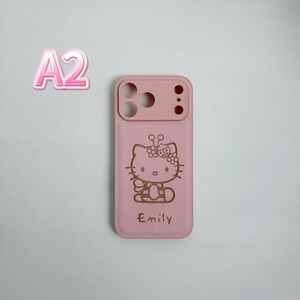 May include: A pink phone case with a Hello Kitty design, a bow, and the name "Emily" engraved. The case has a lighter pink section at the top for the camera. The case is designed for a smartphone.