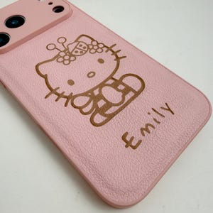 May include: A pink phone case with a brown cartoon cat illustration and the name "Emily". The case has a textured finish and a camera aperture. The design is reminiscent of a popular cartoon character.