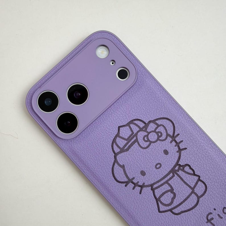 May include: A lilac phone case with a Hello Kitty design. The case has a textured finish and a camera module with three lenses and a flash. The Hello Kitty graphic is in black outline.