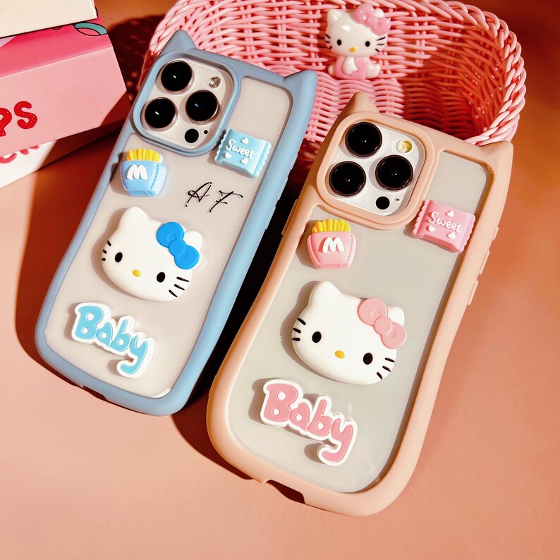 Op de afbeelding: Twee telefoonhoesjes met een transparante achterkant en een zacht, flexibel siliconen frame. De hoesjes zijn versierd met Hello Kitty-figuren, de woorden "Baby" en "Sweet", en andere kleine details. De hoesjes zijn verkrijgbaar in blauw en roze.