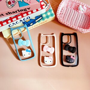 Puede incluir: Tres fundas transparentes para tel&eacute;fono con dise&ntilde;os de Hello Kitty. Las fundas son de color azul, rosa y negro. Cada funda tiene una cara de Hello Kitty y un lazo.