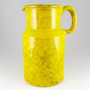以下が含まれることがあります： 明るい黄色のセラミックピッチャー、ハンドル付き。ピッチャーは光沢のある仕上げとテクスチャ加工された表面を持っています。ピッチャーは円筒形で、わずかにフレアしたベースと注ぎ口があります。